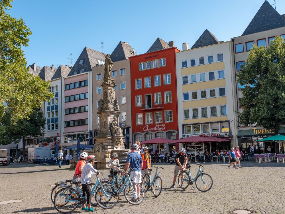 Reiseleiter mit einer Gruppe von Touristen in Köln bei einer geführten Radtour am Alter Markt